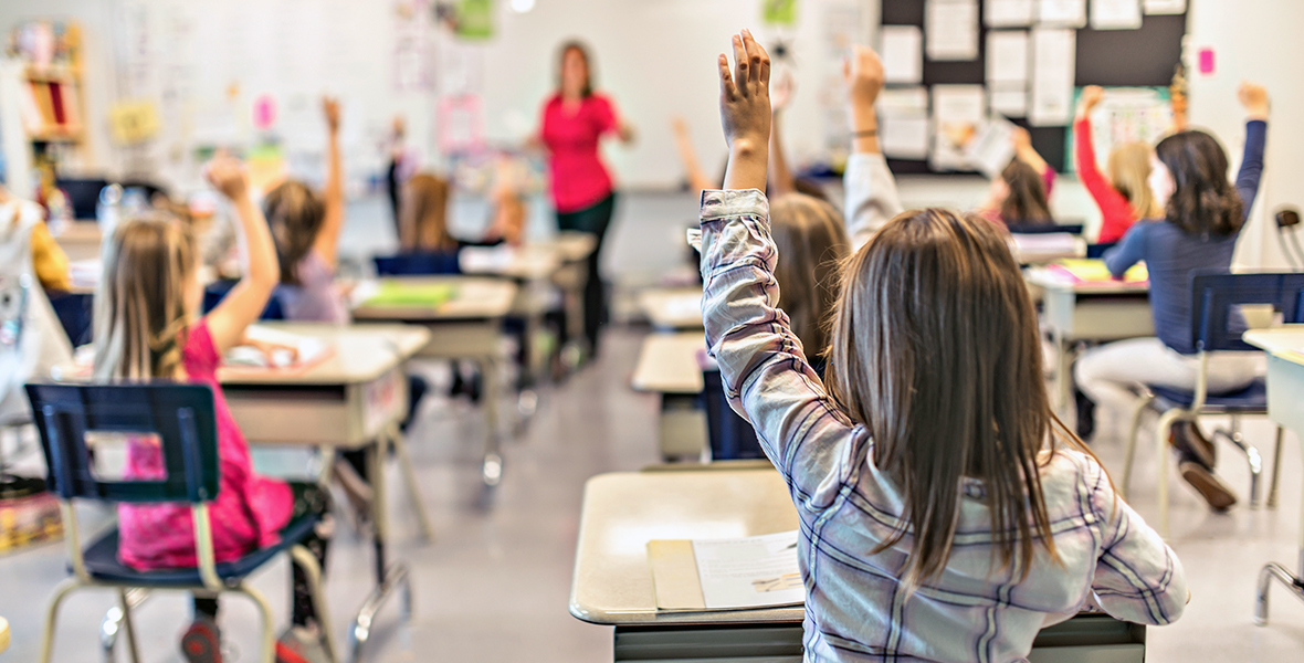 Elementary school classroom with engaged students raising their hands to participate. Supportive learning environment promoting confidence, curiosity, and children's mental well-being.